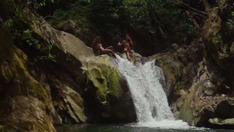 having fun and enjoying a tropical waterfall in the caribbean: two girls in bikinis.