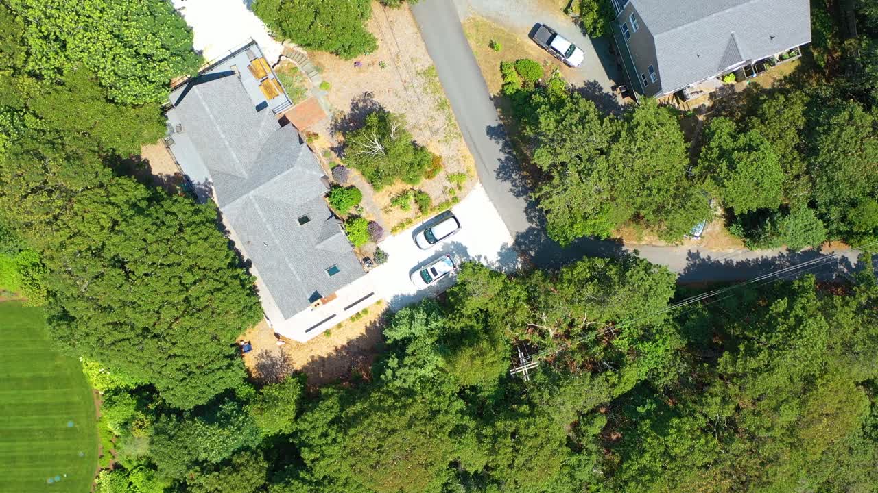Drone footage begins at ground level and ascends to a top-down aerial view of residential homes, driveways, and tree-lined streets, revealing the surrounding neighborhood and greenery from above