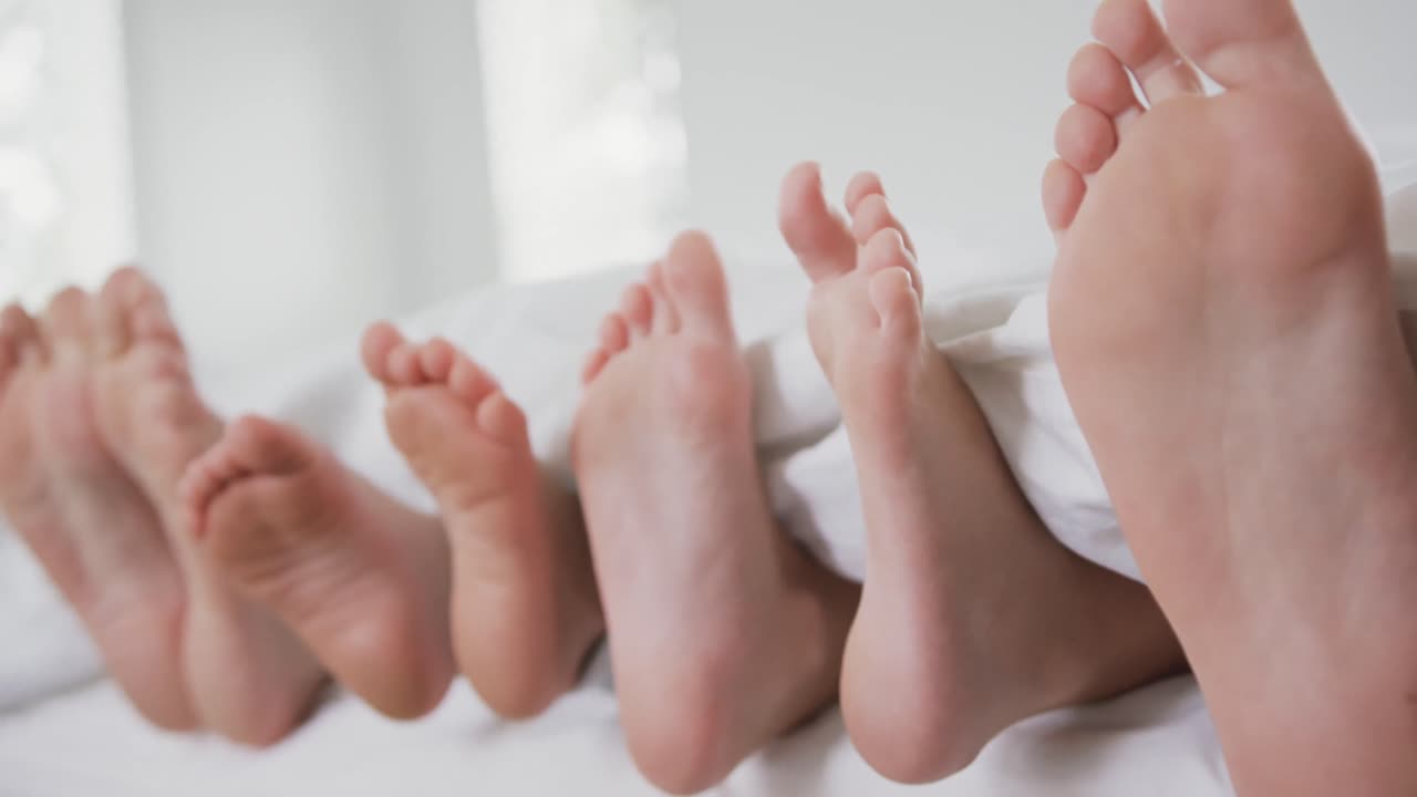 Pies de familia bajo la manta en la cama del dormitorio de un hogar cómodo 4k