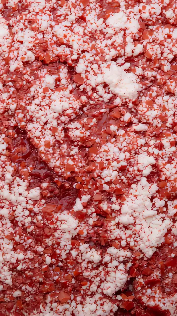 Vertical video: Shifting camera revealing glossy red paste surface, macro, white clumps shifting