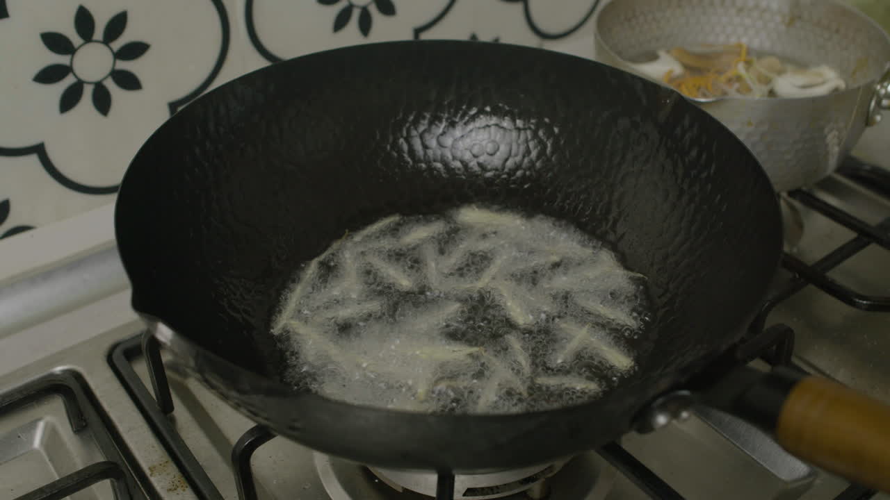 Adding potato shreds into hot oil inside big Asian frying pan