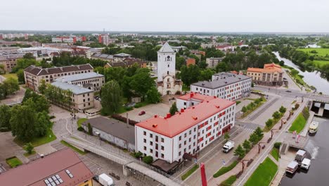 Grey skies cover Jelgava riverside with vibrant buildings, historic tower view