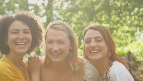 portrait of three female friends sitting outdoors in summer garden at home relaxing and talking