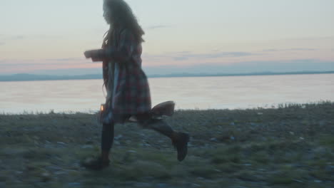 young woman holding glowing lantern, running along lakeside at dusk