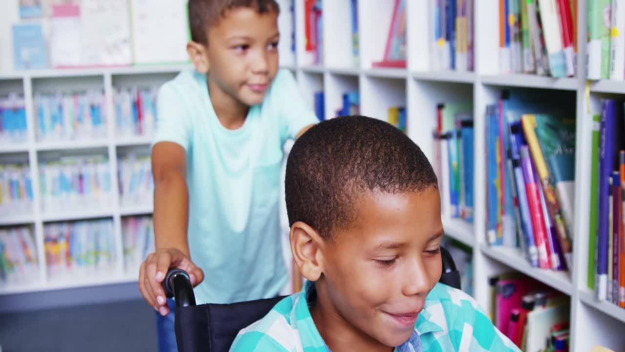 Happy schoolboy carrying his friend in wheelchair at library