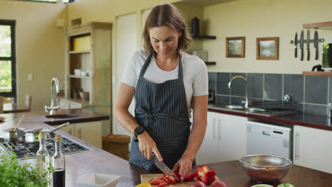 happy caucasian pregnant woman wearing apron and cutting red pepper