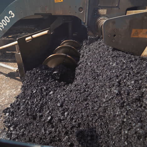 metal construction of a heavy paver machine pouring out hot asphalt on the road. asphalt spreader at work. large truck laying black bitumen. close-up.