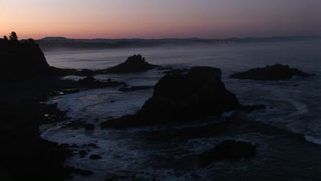 Una-Amplia-Franja-De-Cielo-Rosa-Y-Naranja-Ilumina-Este-Metraje-De-Una-Costa-Rocosa-Gris