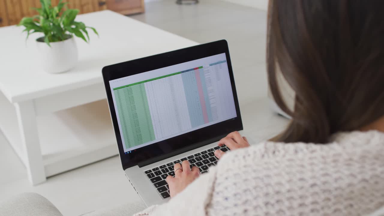 Back view of asian woman sitting on sofa and working remotely from home with laptop