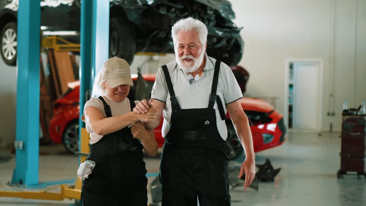 trabajadores mecánicos alegres se divierten en el trabajo. una mujer adulta y un viejo mecánico están riendo y divirtiéndose con herramientas en el garaje