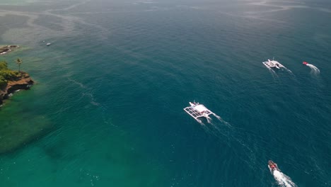 Local-fishing-boats-sail-on-ocean-aerial-reveal-of-island-coast,-Philippines