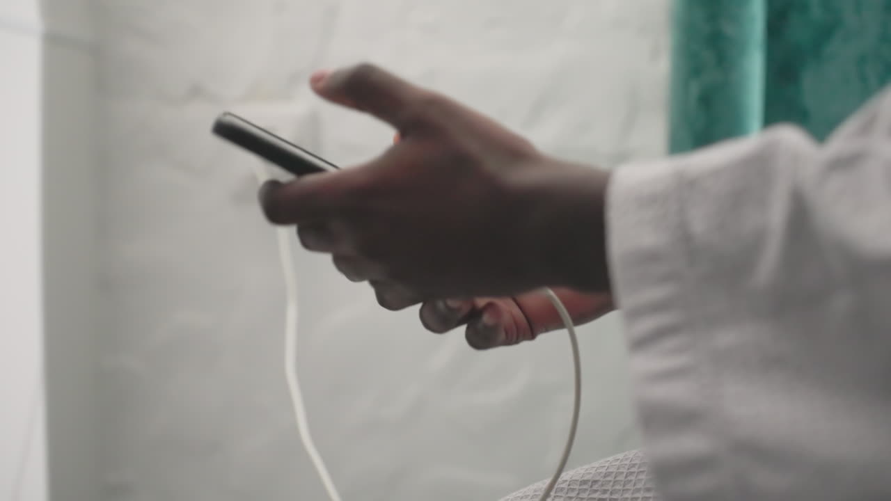 African man plugging charger into outlet in bedroom. Modern room with cozy ambiance, minimalist design. Hand reaching out to connect device to electricity. Calm morning routine moment