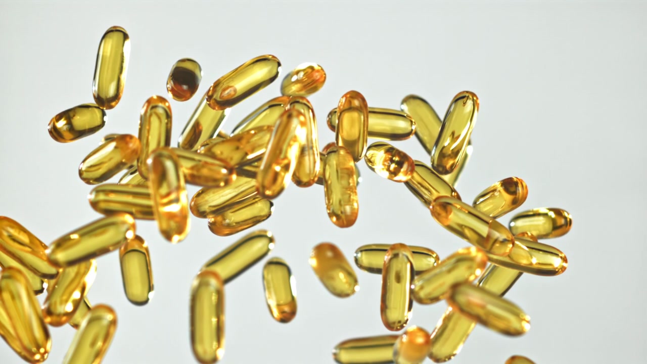Capsule di olio di pesce Omega-3 dorate che fluttuano verso l'alto su sfondo bianco