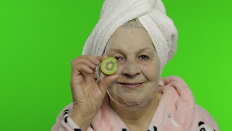 elderly grandmother in bathrobe with bubble face mask. old woman with kiwi