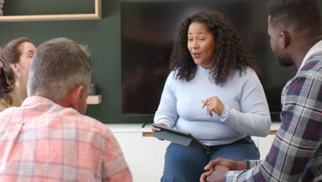 Diverse-group-of-friends-and-female-therapist-with-tablet-in-group-therapy-session