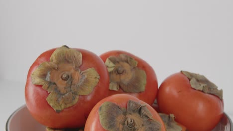 Panning-down-from-bowl-of-persimmons-close-up-of-asian-persimmons-in-a-bowl-showing-stems-and-vibrant-color