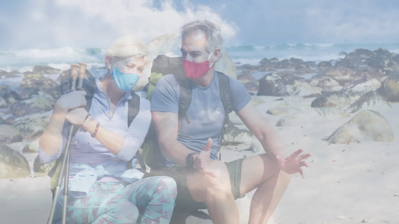 행복 한 백인 노인 부부 가 해안 에서, 빠르게 움직이는 구름 위 에서 하이킹 하고 있다