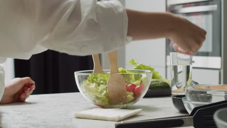 맛있는 아보카도 샐러드에 다양한 씨앗을 추가하고 나무 주걱으로 유리 그릇에 섞는 여성의 손을 닫습니다
