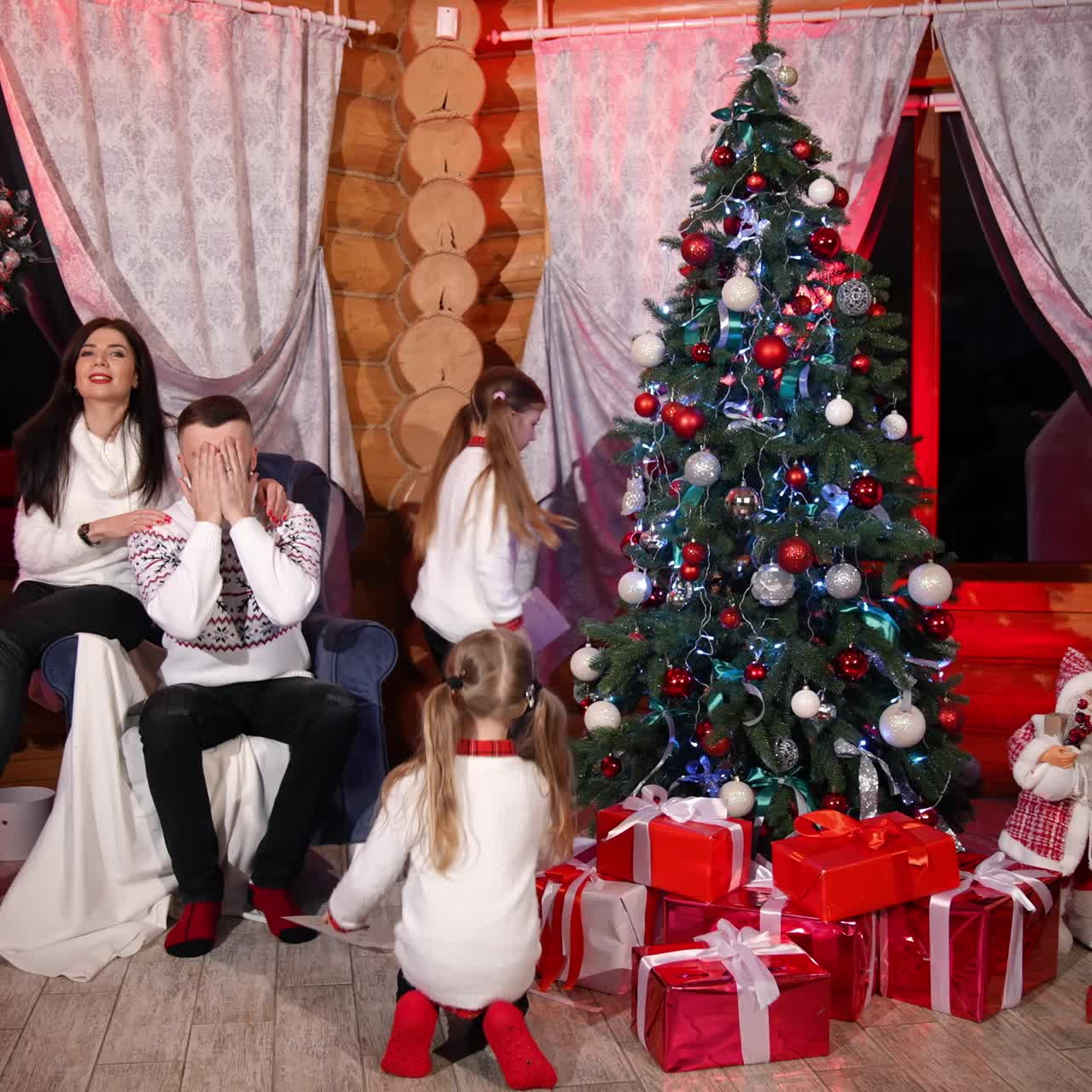 Surprise. Full length view of the young parents closed their eyes while waiting for the presents from their daughters. Family celebrating New Year