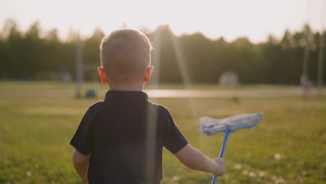 toddler boy runs holding butterfly net along meadow