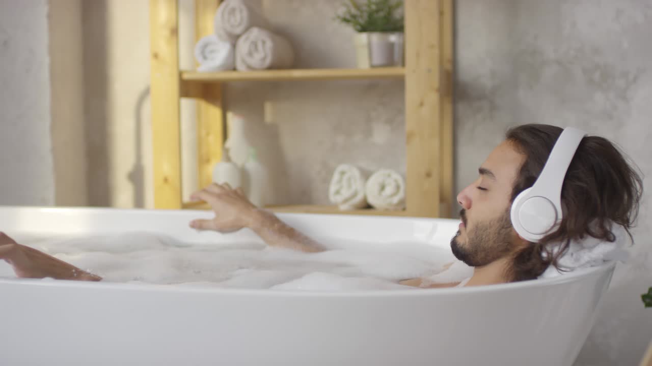 Man Resting in Bath and Listening to Music with Headphones