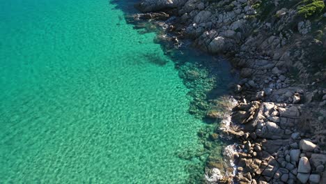 Toma-Aérea-De-Un-Acantilado-Rocoso-Y-Hermosas-Aguas-Turquesas-Claras-En-El-Sur-De-Cerdeña,-Italia