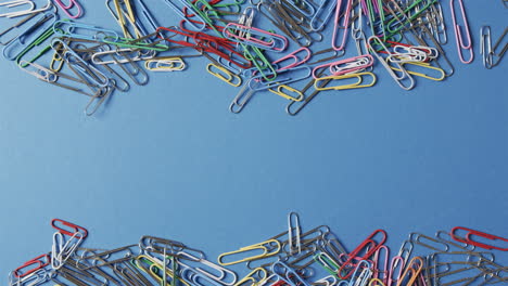 colorful paper clips are scattered across a blue background, with copy space