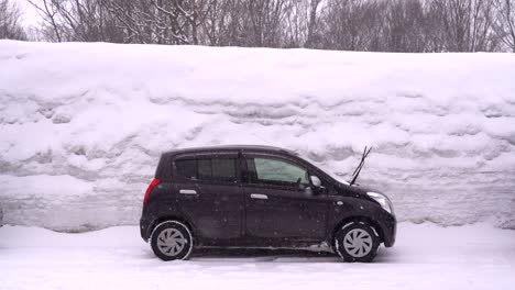 Schwarzes-Auto,-Das-Gegen-Eine-Sehr-Hohe-Schneewand-Geparkt-Ist,-Wobei-Der-Schnee-In-Zeitlupe-Fällt