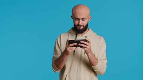 joyful muslim man playing mobile video games in studio