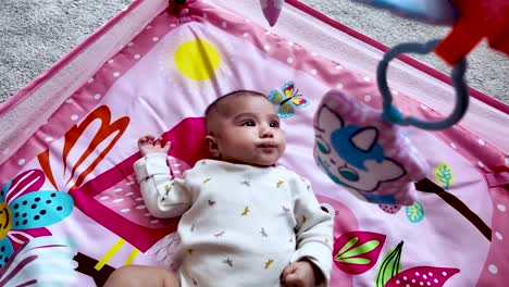 cute infant lying on a colorful pink play mat with attached hanging toys. slow motion, bird eye view