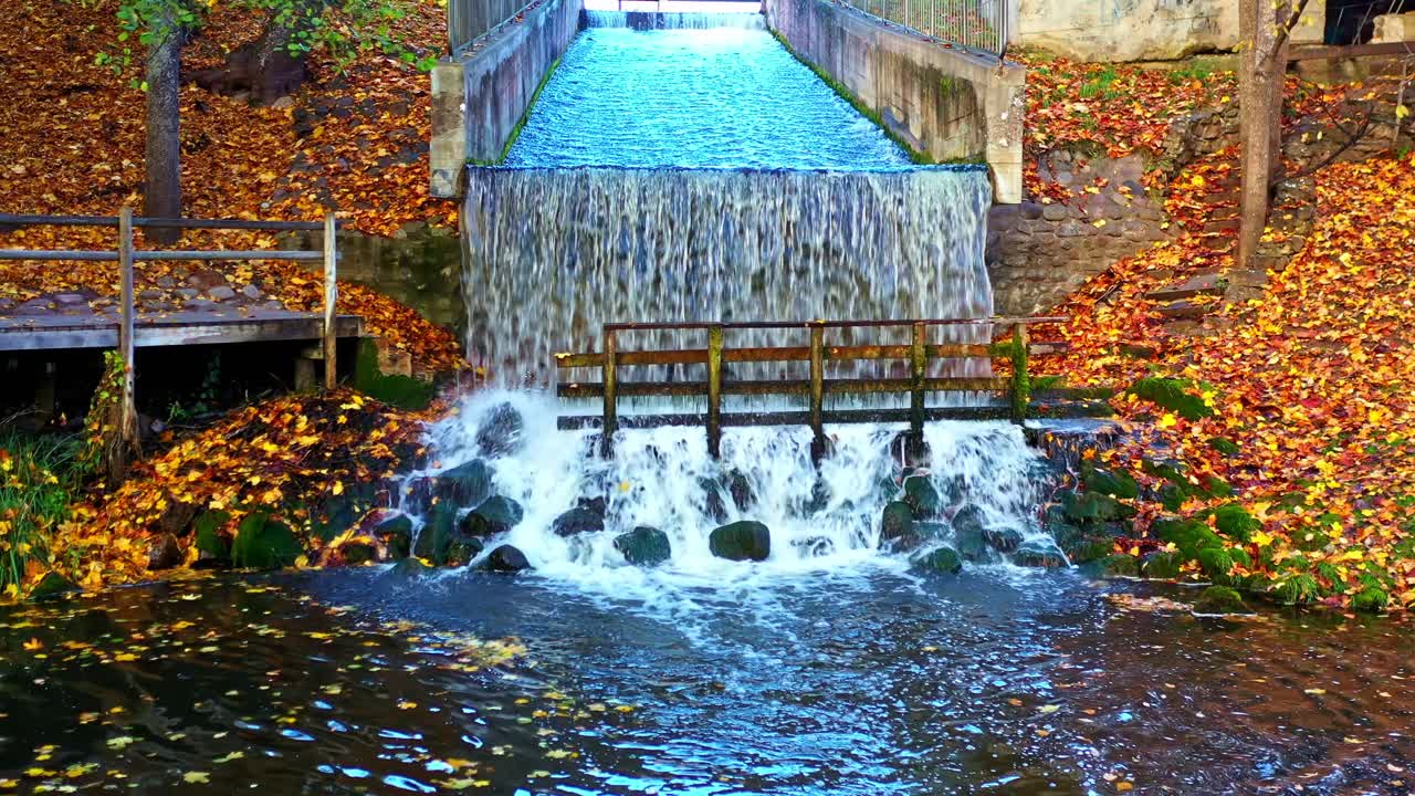 Acqua che scorre su una struttura di sbarramento in cemento creando una cascata tra le foglie autunnali