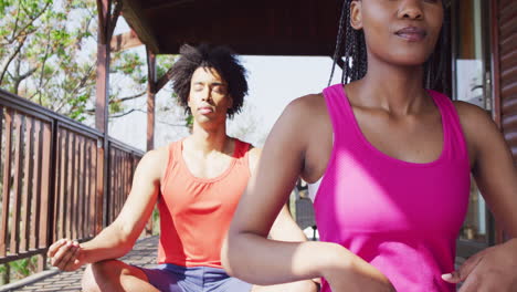 happy african american couple doing yoga and meditating in log cabin, slow motion