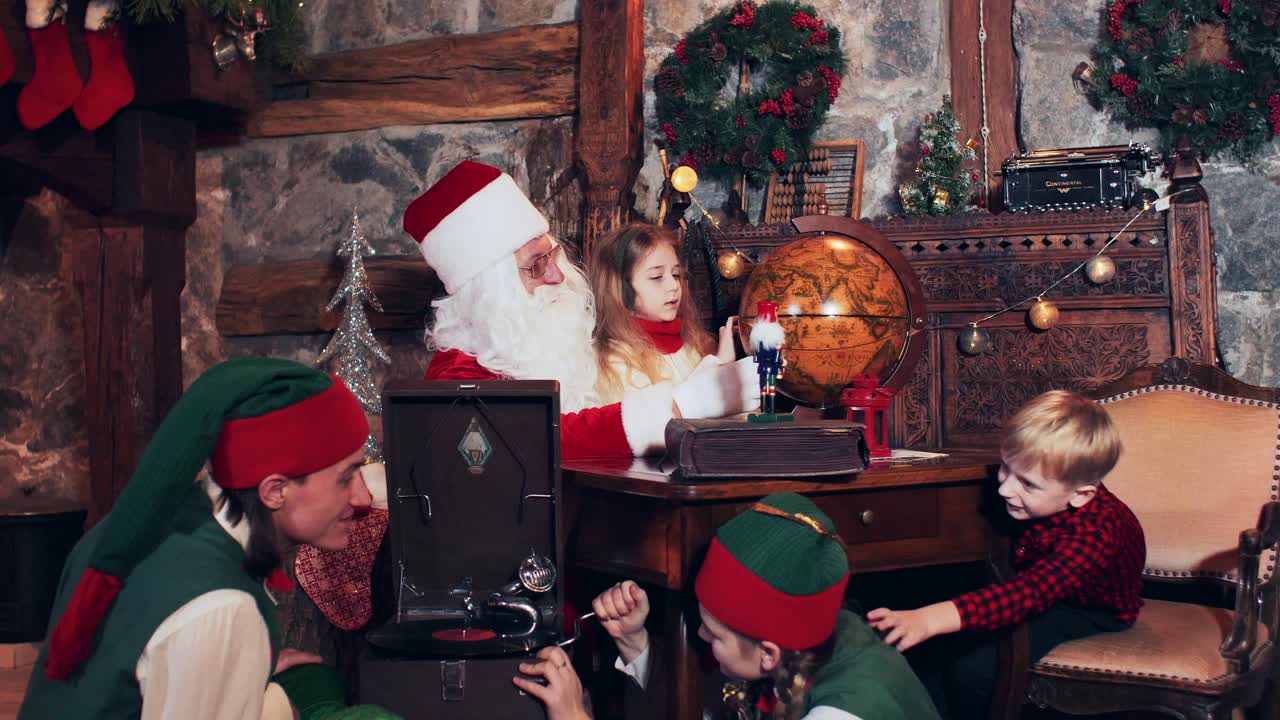 Santa Claus and children are exploring the country on a retro globe. Christmas elves sitting on the floor set up an old gramophone