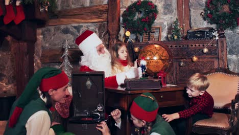 santa claus and children are exploring the country on a retro globe. christmas elves sitting on the floor set up an old gramophone