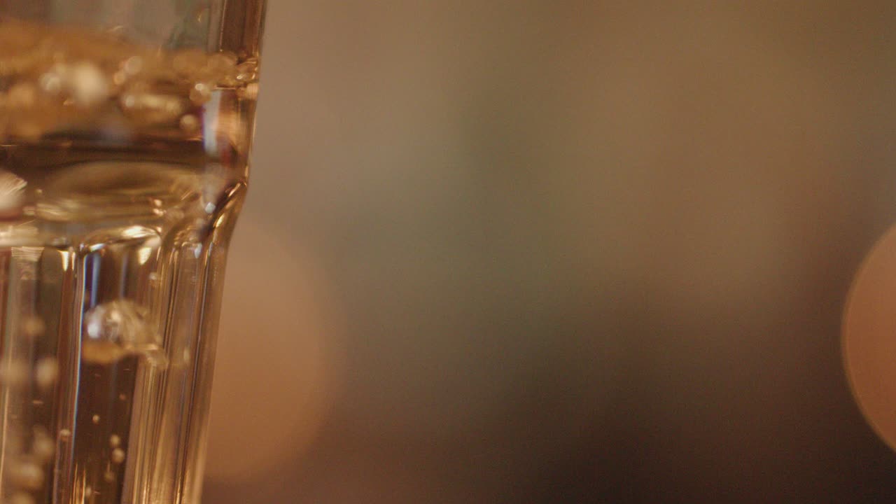 A clear glass of water stands still on a table in a softly lit restaurant at night, with warm bokeh background and minimal camera movement