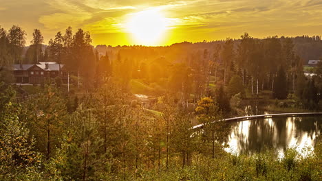 golden sunset behind forest trees in idyllic scenery with lake and holiday apartments - time lapse