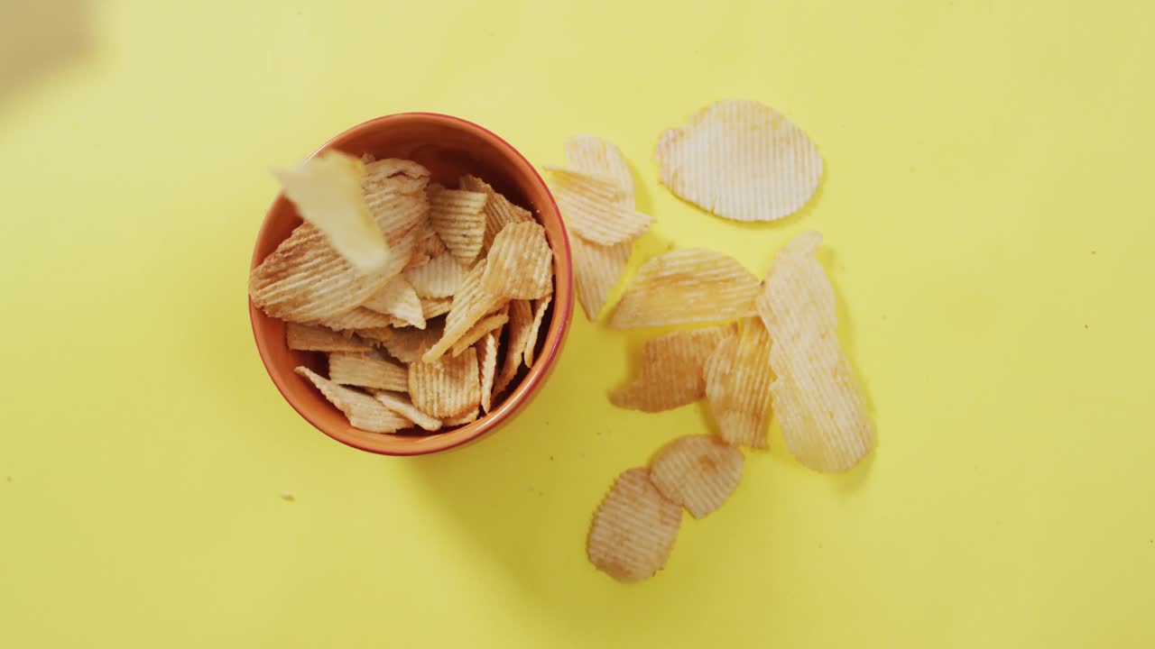 Primo piano di patatine fritte che cadono in una ciotola con spazio per il testo su superficie gialla.