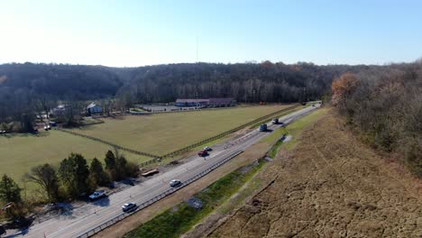 aerial shot of cars driving along a rural highway between some fields and forests on a sunny, winter day