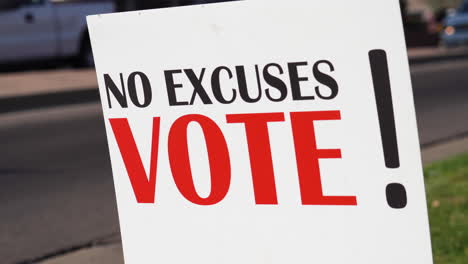 political voter rally sign next to road with cars driving by close up, no excuses vote