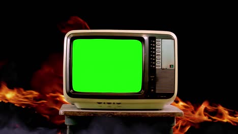 old television set with green screen amidst flames and fire. zoom in. 4k resolution.