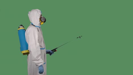 side view disinfection man with special white suite and a respirator sprays antiseptic solution on a green screen, chroma key. slow motion. close up