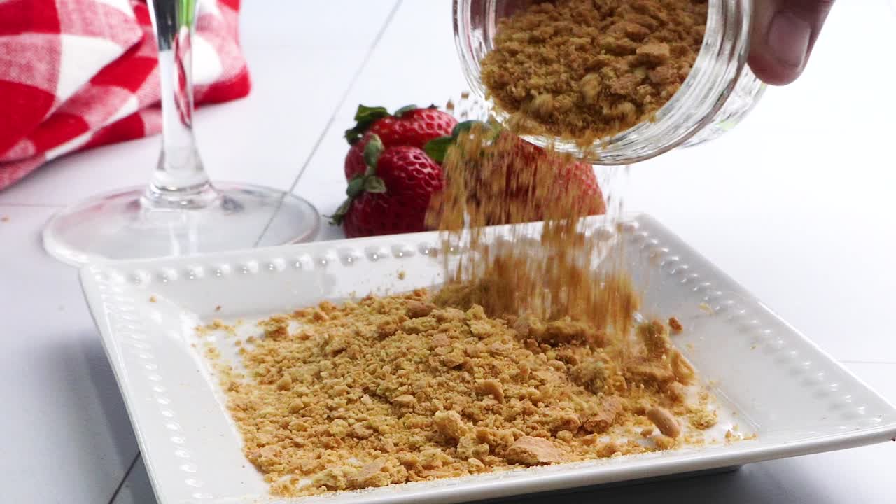 Pouring crushed graham crackers out of a mason jar unto a white plate. Using graham crackers to rim a cocktail glass. Close up of graham crackers on a plate.