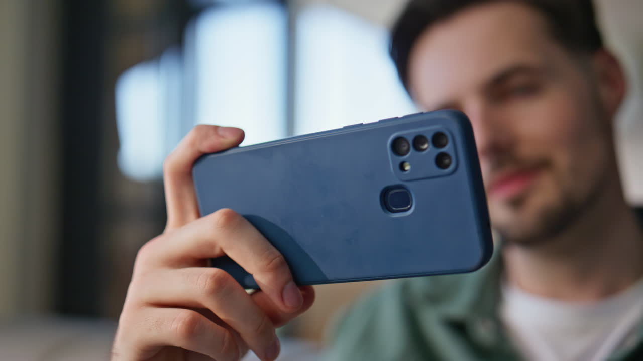 Positive guy watching video on smartphone at home closeup. Man looking screen