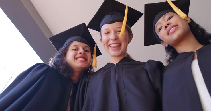 Female grads with child at door wearing gowns gold tassel caps raising rolled diplomas celebrating