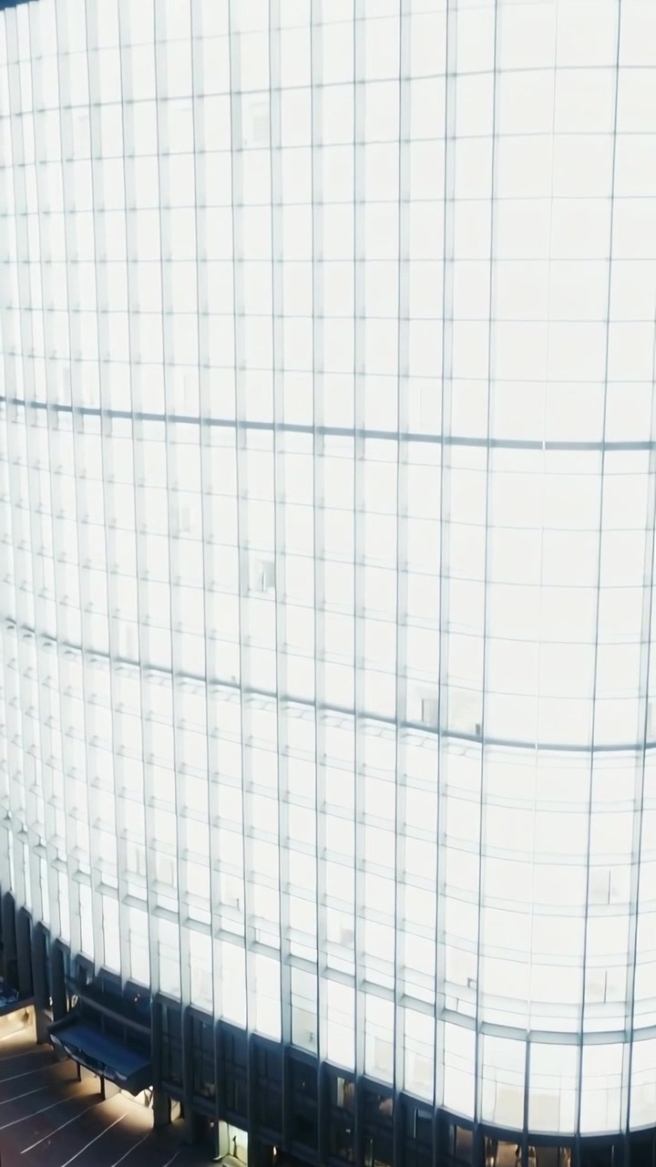 Video verticale: Telecamera che si inclina partendo dal basso, rivelando un edificio di vetro curvo, uffici illuminati al crepuscolo.