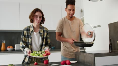 Portrait-of-a-young-Black-skinned-brunette-man-in-a-cream-t-shirt-and-his-young-adult-girlfriend-with-a-bob-hairstyle-they-present-their-breakfast-of-scrambled-eggs-and-fresh-salad-during-their-breakfast-preparation-in-a-modern-kitchen