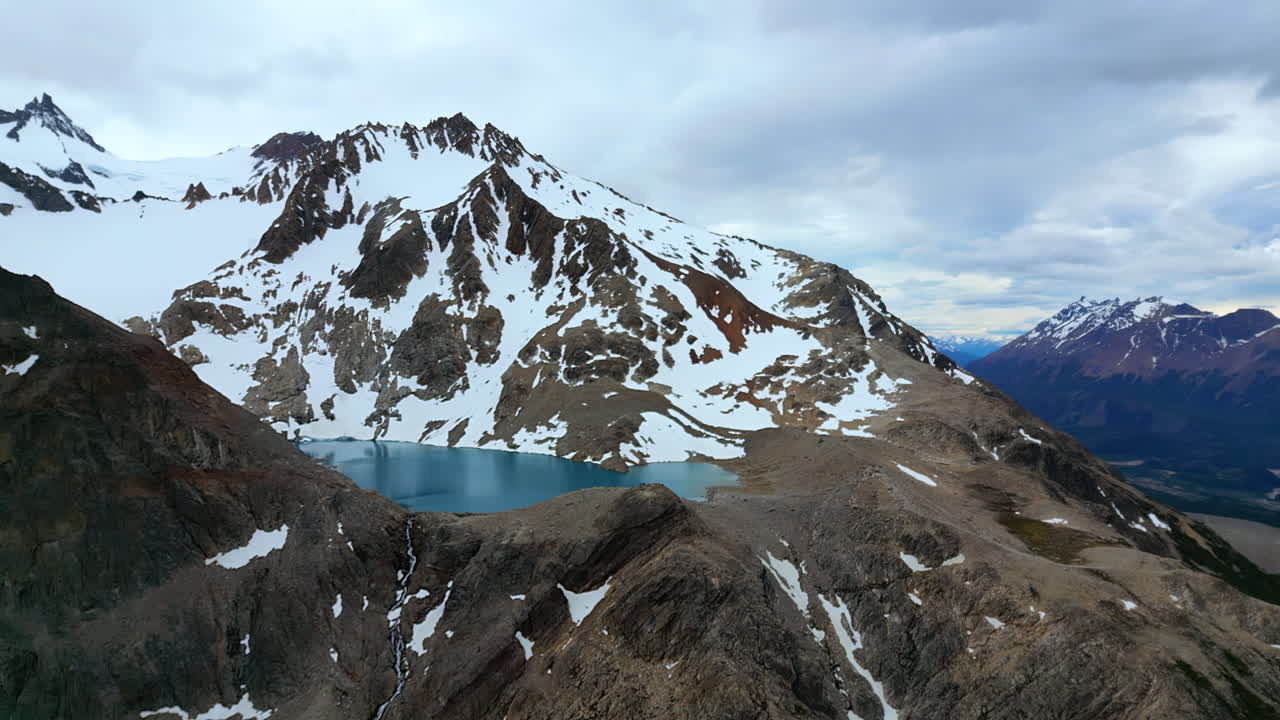 Aerial drone view the vibrant blue, high altitude lake surrounded by snow patches and rocky slopes