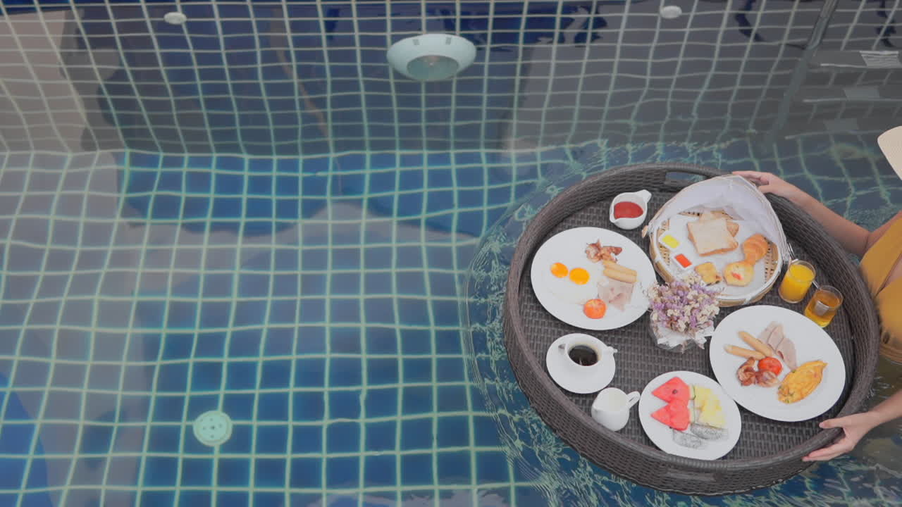 한 젊은 여성의 머리 위가 수영장을 가로질러 떠다니는 아침 식사 음식 연회를 안내합니다.