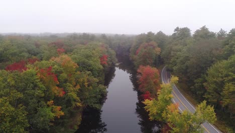 aerial foggy river with autumn foliage flying forward with road beside