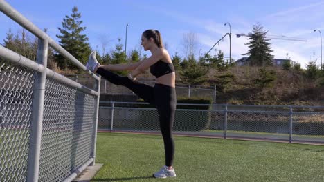 mujer joven atlética flexible estirando la pierna contra la barandilla